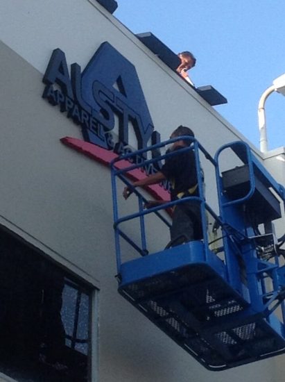 sign repair professionals in a boom lift fixing an outdoor business sign.